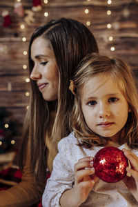 Hispanic mom holding her daughter with red ball and lights. 
