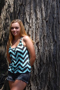 Portrait of young woman leaning on tree trunk