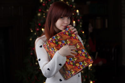 Portrait of young woman holding gift box at home