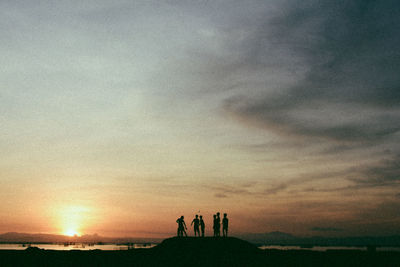 Silhouette people standing on landscape against sky during sunset