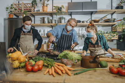 Chefs team wearing protective face mask cooking while working together in kitchen