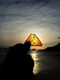 Close-up of silhouette hand against sea at sunset