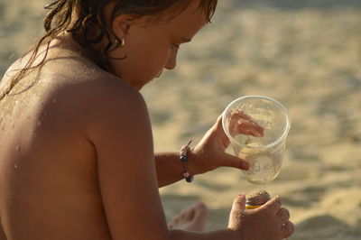 Side view of shirtless girl on playing with sand on shore of beach