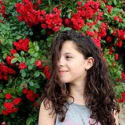 Teenage girl with brown hair against red roses blooming outdoors