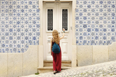 Rear view of woman with backpack knocking door