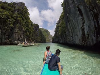 Rear view of people sitting on boat in sea amidst cliffs