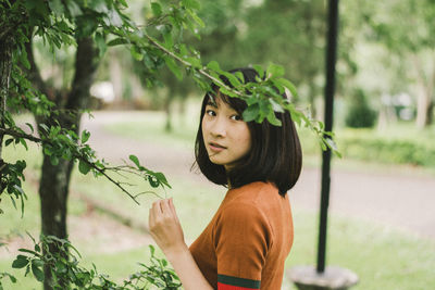 Portrait of young woman standing by plants in park