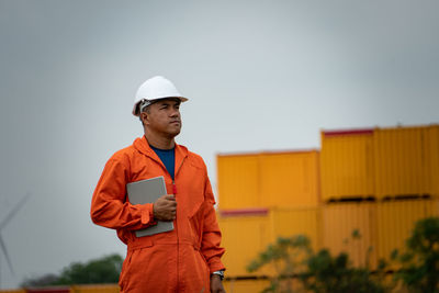 Man holding digital tablet while looking away against sky