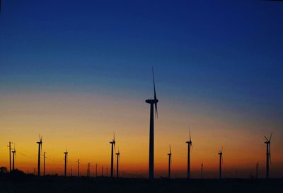 Silhouette wind turbines on field against sky during sunset