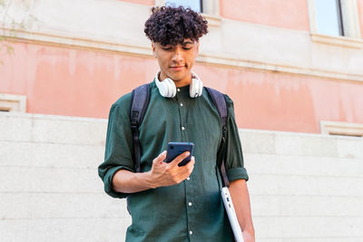 Ethnic man with headphones looking at screen of modern mobile phone on the street