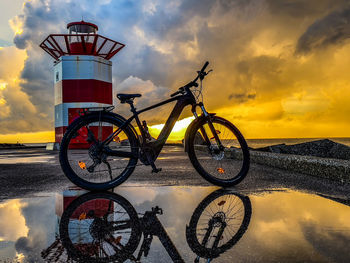 Bicycle wheel on beach against sky during sunset