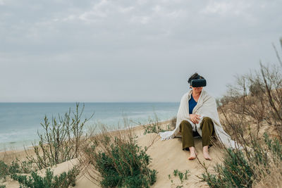 An adult woman on a sandy beach in spring wearing vr virtual reality glasses in front of her eyes