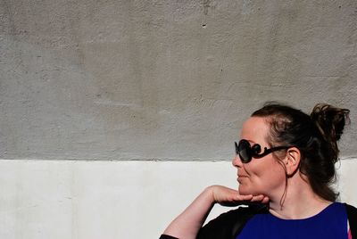 Woman wearing sunglasses against wall