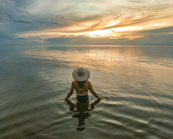 Full length of woman in sea against sky during sunset