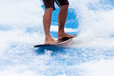 Low section of man surfing on sea