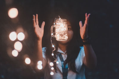 Woman with illuminated string lights in jar standing outdoors