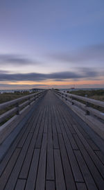 Surface level of boardwalk against sky during sunset