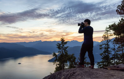 Man photographing on mountain against sky during sunset