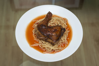 High angle view of chicken with spaghetti in plate on glass table