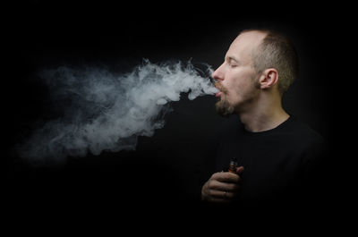 Young man smoking against black background