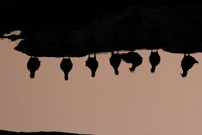 Reflection of silhouette rocks on water against sky