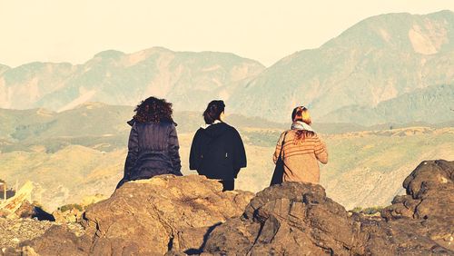 Rear view of women sitting on rock formations against mountains