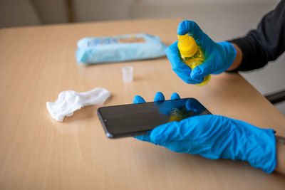 Hand in gloves sanitizing cleaning smartphone mobile phone on table surface with wet wipes alcohol