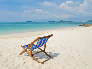 Deck chairs on shore at beach against sky