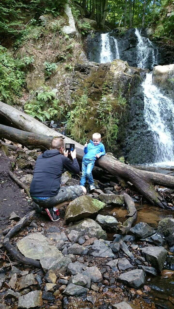 water, lifestyles, leisure activity, rock - object, full length, men, nature, rear view, high angle view, casual clothing, day, river, childhood, outdoors, travel, rock, forest, log