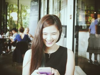 Happy young woman text messaging while sitting at restaurant