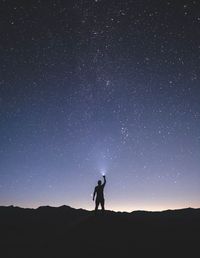 Silhouette man holding flashlight while standing on mountain against star field at night