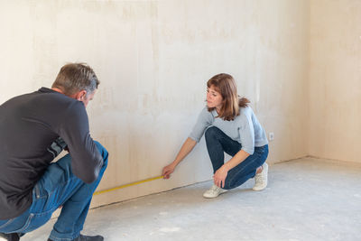 Young couple moving in new apartmen. people measure size of wall with tape measure. concept new 