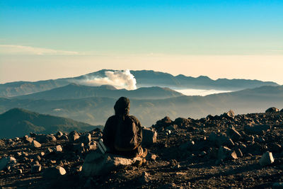 Rear view of person sitting on rock against mountain and sky