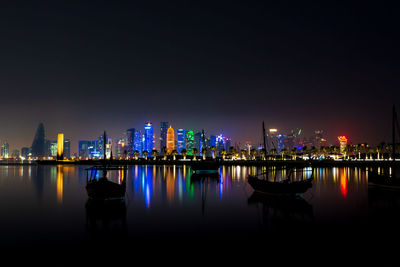 Illuminated buildings by river against sky at night
