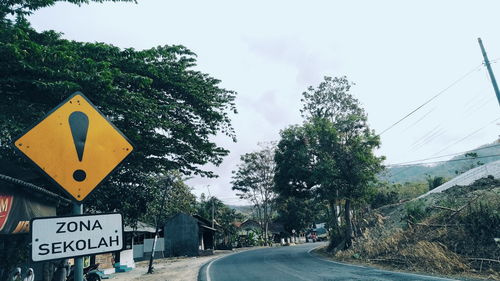 Road sign by trees against sky