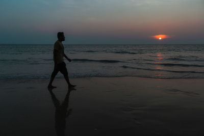Silhouette man walking on beach against sky during sunset