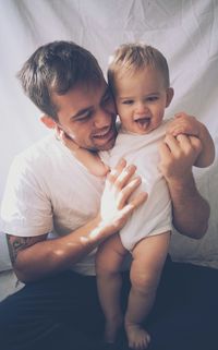 Smiling man holding his son while sitting on bed