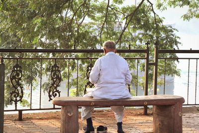 Rear view of man sitting on bench against railing at park