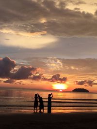 Silhouette men standing on beach against sky during sunset