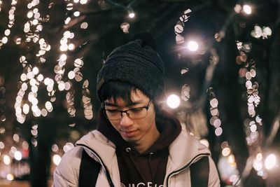 Portrait of man with illuminated christmas tree at night