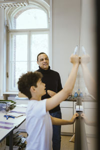 Male teacher looking at student writing on whiteboard in classroom