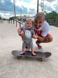 Father-to-son skateboarding, bald man  holding the hands of his son over his skateboard.