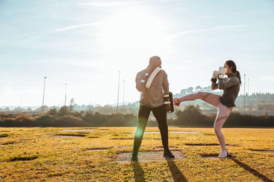 Full length of woman and man exercising on field against sky