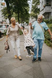 Playful grandparents enjoying with granddaughter while walking on footpath at street