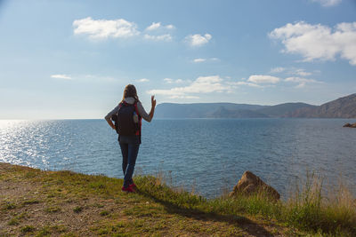 A young female traveler. a girl with a backpack is standing on the seashore. beautiful spring 