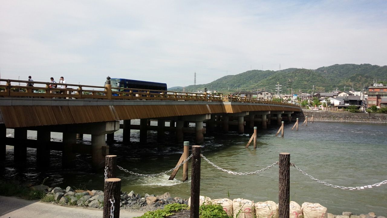 architecture, built structure, water, sky, building exterior, mountain, railing, bridge - man made structure, sea, river, connection, cloud - sky, transportation, outdoors, day, pier, cloud, incidental people, house, nature