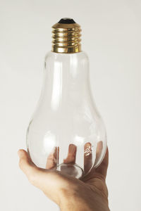 Close-up of hand holding glass bottle against white background