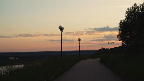 Street amidst trees against sky during sunset