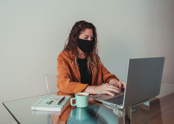 Woman wearing mask working on laptop at home