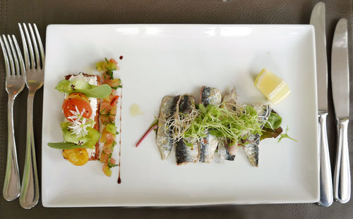 Directly above shot of sardines and open faced sandwich vegetables served on table